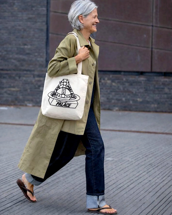 Femme de plus de 60 ans portant un trench kaki long, un jean droit retroussé et des sandales plates