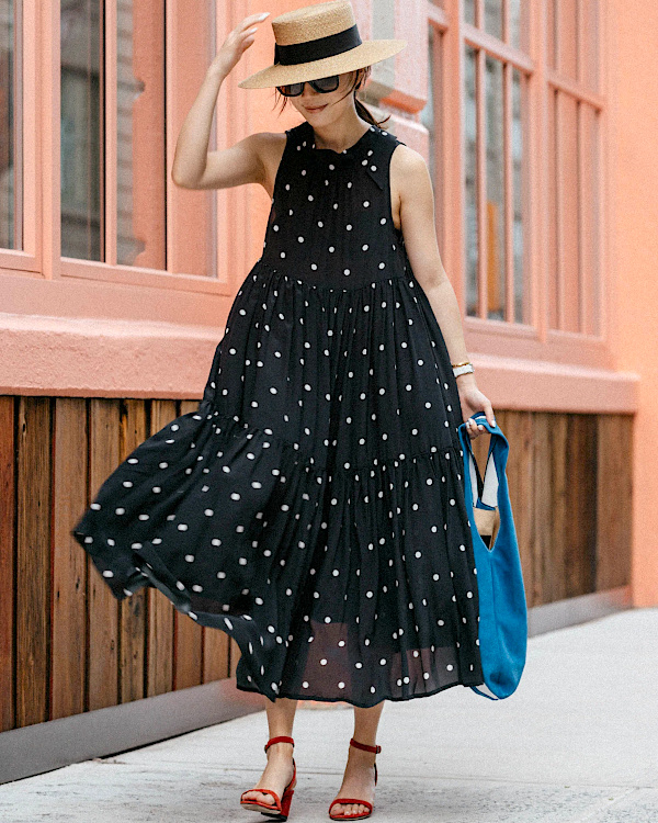 Robe noire à pois blancs fluide portée avec chapeau de paille et sandales rouges