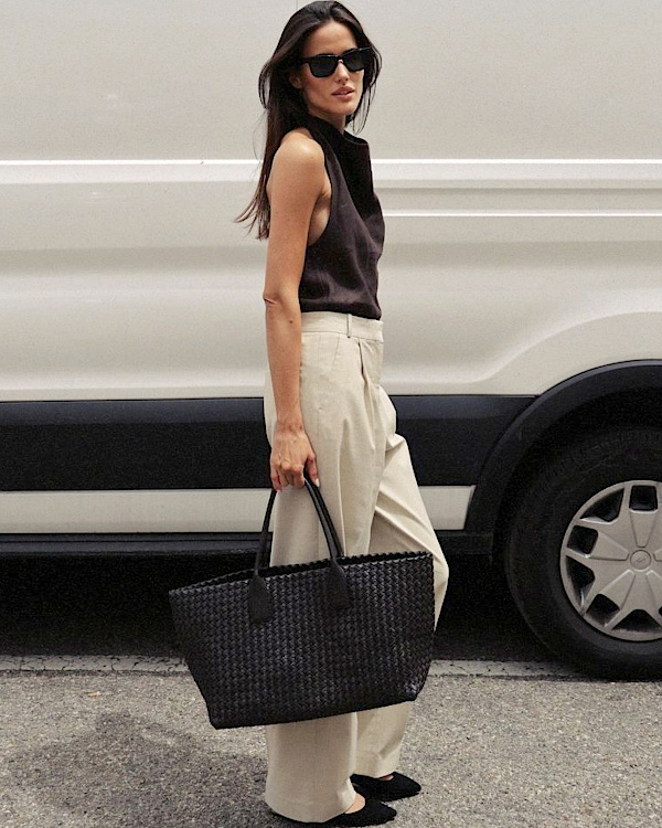 Look estival professionnel avec top sans manches noir, pantalon clair large et sac tressé